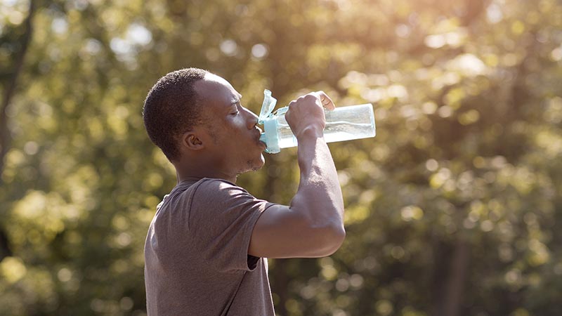 Man drinks from a water bottle in the heat outside